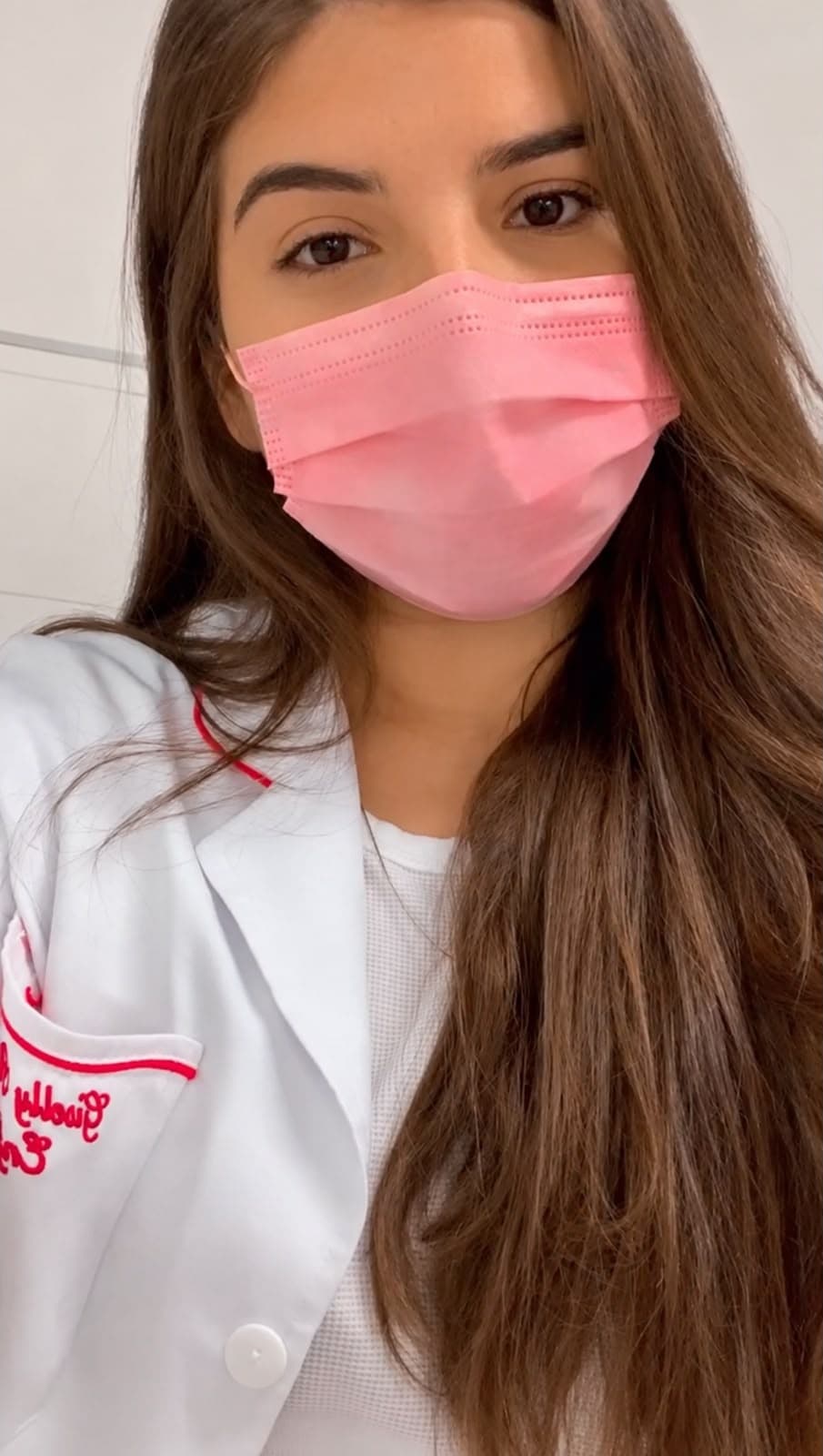 Giselly na época da faculdade de enfermagem, de uniforme branco e máscara rosa.