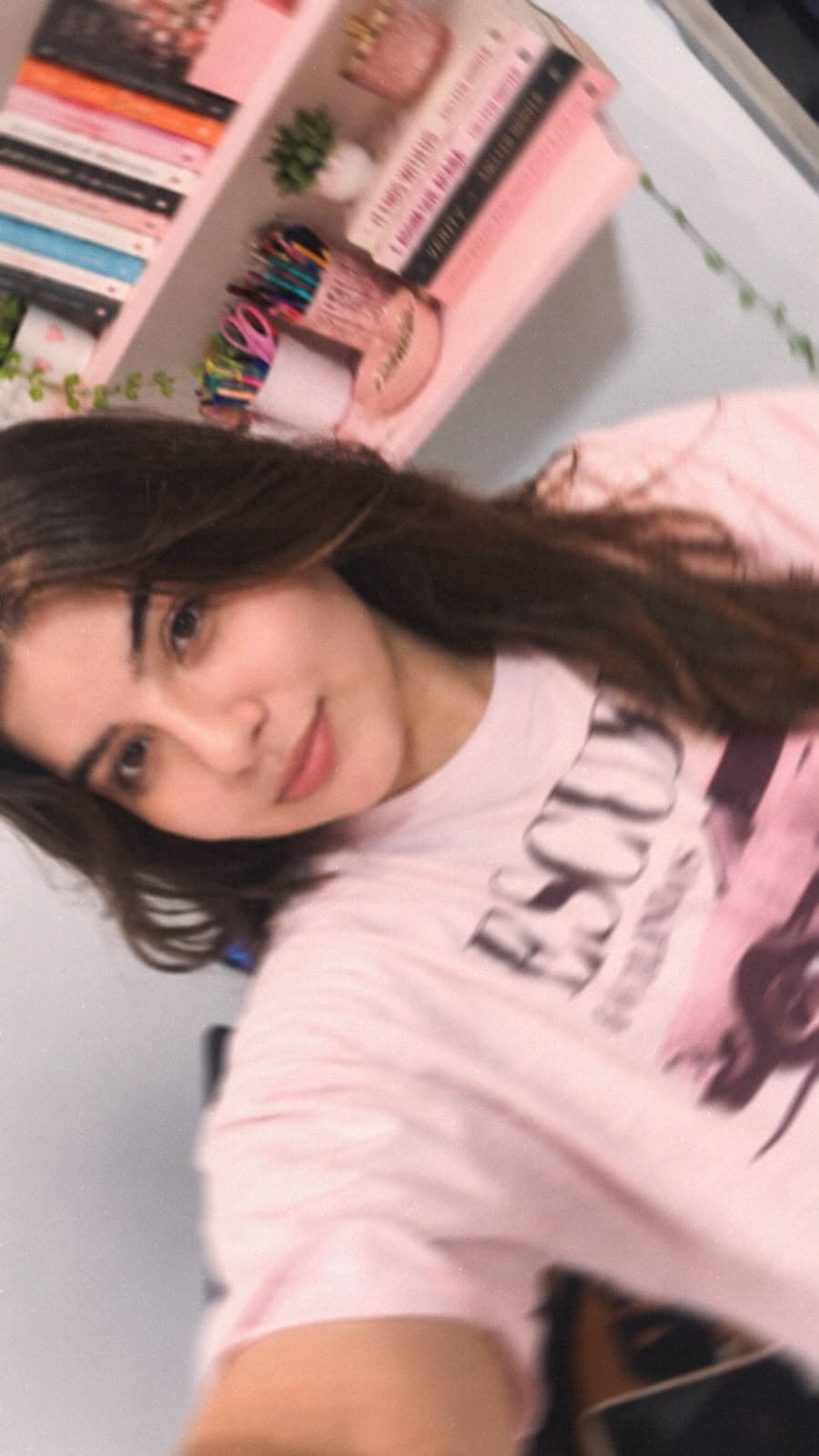 Giselly de camiseta rosa, ao lado de uma estante de livros.