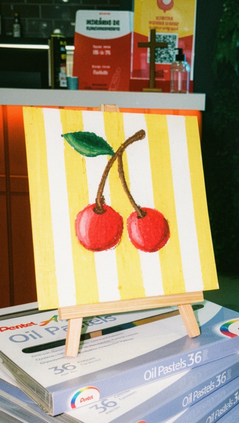 Pintura de duas cerejas sobre listras amarelas, apoiada em um pequeno cavalete.